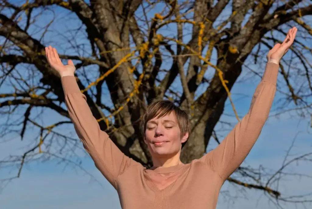 Dorothee Hildbrand steht mit erhobenen Armen aufrecht vor einem Baum. Souverän und gelassen.