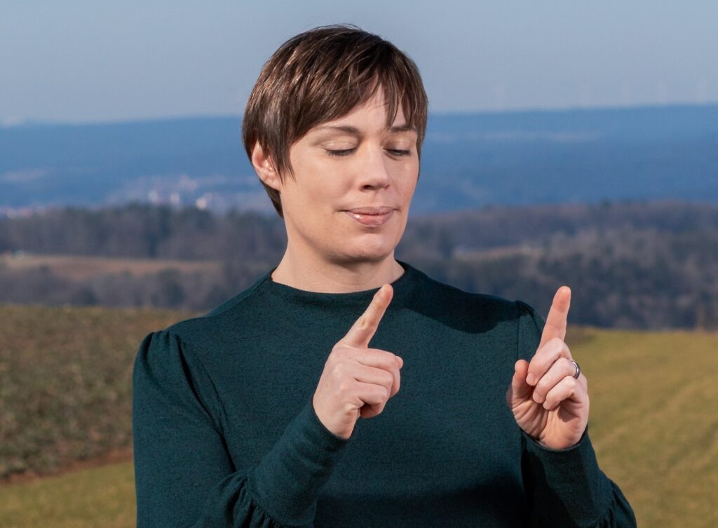 Dorothee Hildbrand steht in der Natur und zeigt mit den Fingern einen kleinen Abstand – Symbol für: „Es braucht nicht viel Zeit, um ins Handeln zu kommen“