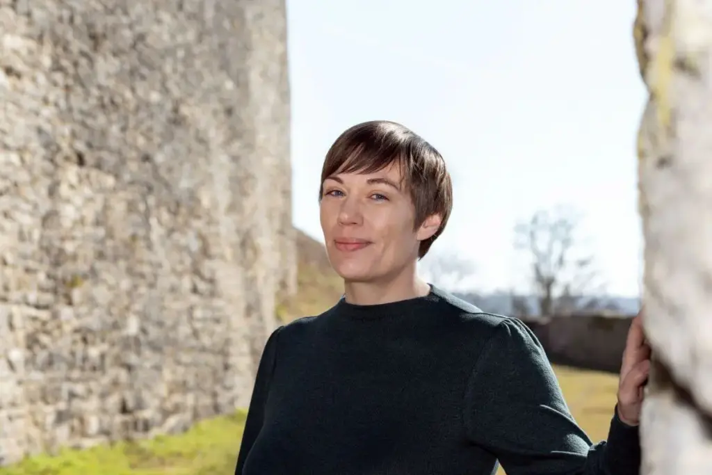 Dorothee Hildbrand draußen an einer Natursteinmauer – steht für ganzheitliches Coaching, das flexibel, sicher und individuell an Alltag, Tempo und Thema angepasst ist