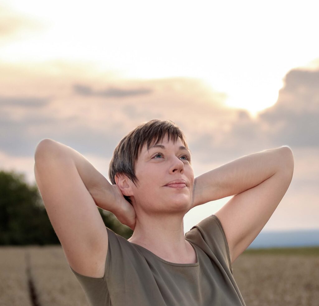 Frau im Sonnenuntergang, die ihre Arme ausbreitet. Darauf steht der Text: Ich bin gut, wie ich bin – positive Botschaft gegen Selbstzweifel und für Selbstvertrauen.