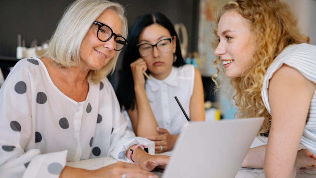 3 Frauen im Businesskontext sitzen souverän am Tisch und diskutieren.